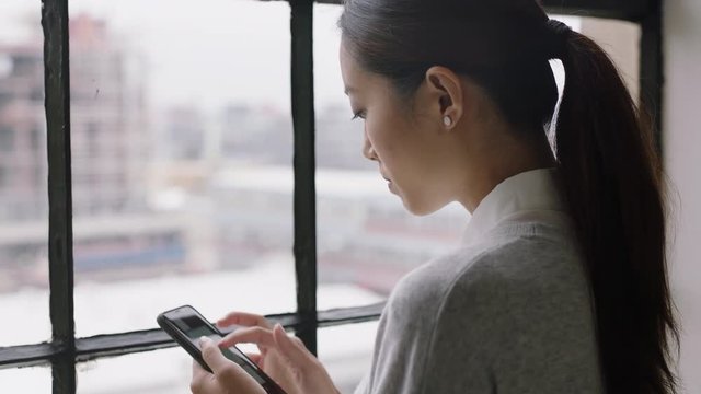 beautiful asian business woman drinking coffee at home using smartphone enjoying relaxed morning browsing messages looking out window planning ahead texting on mobile phone networking