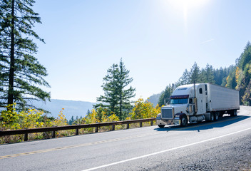 Fototapeta na wymiar Big rig white classic semi truck transporting cargo in refrigerated semi trailer on winding autumn road