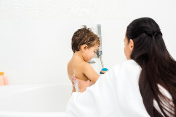 Mother with long hair washing son in white bathroom