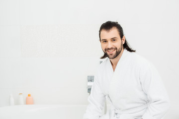 Handsome man smiling in bathrobe in white bathroom