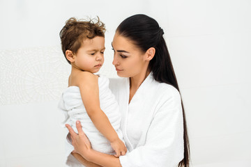 Mother looking at toddler son with closed eyes on white