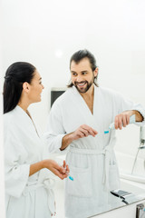 Fototapeta premium happy couple in white bathrobes brushing teeth together