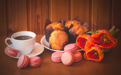 Cup of coffee,  macaroon cookies, tulip flowers and vanilla muffins on wooden table. Selective focus.