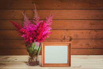 Wooden frame and beautiful astilbe flowers in glass vase on wooden table. View with copy space.