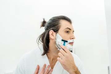Handsome man in bathrobe shaving in bathroom