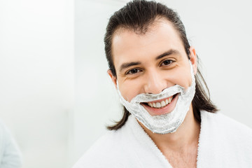 Man with shaving foam on beard smiling in bathroom