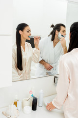 beautiful woman brushing teeth and handsome man shaving in front of mirror in bathroom