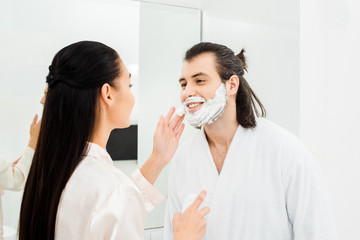 Handsome man smiling while woman applying shaving foam on man face
