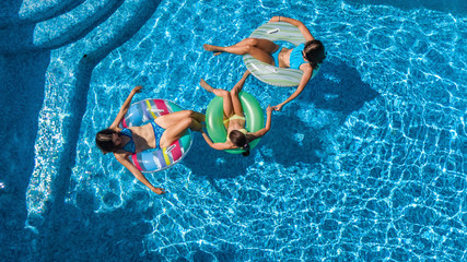 Family in swimming pool aerial drone view from above, happy mother and kids swim on inflatable ring donuts and have fun in water on family vacation, tropical holidays on resort
