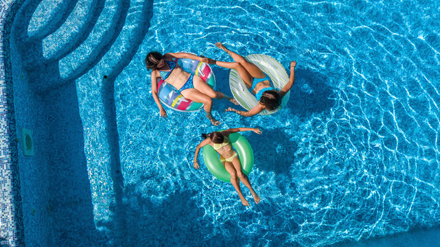 Family in swimming pool aerial drone view from above, happy mother and kids swim on inflatable ring donuts and have fun in water on family vacation, tropical holidays on resort
