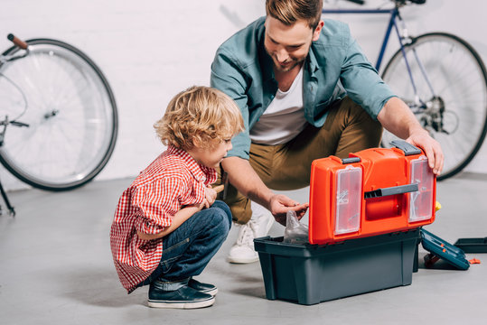 father and adorable little son sitting near opened tools box in bicycle workshop