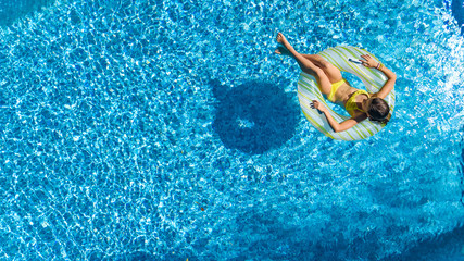 Aerial drone view of little girl in swimming pool from above, kid swims on inflatable ring donut , child has fun in blue water on family vacation resort
