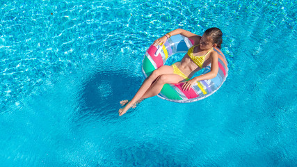 Aerial drone view of little girl in swimming pool from above, kid swims on inflatable ring donut ,...