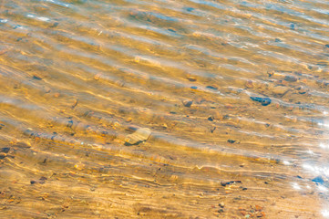 Ripples on water. Yellow sand beneath the clear water, view from above