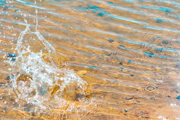 A splash of clean water from a fallen stone. Ripples on water.  Yellow sand beneath the clear...