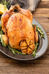 Whole roasted chicken with lemon and rosemary on a black plate. Rustic style. Christmas concept. Christmas turkey.