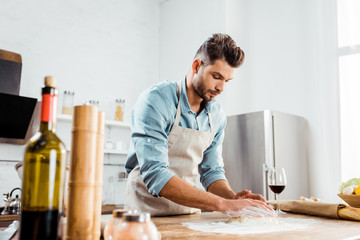 low angle view of focused young man in apron preparing dough in kitchen