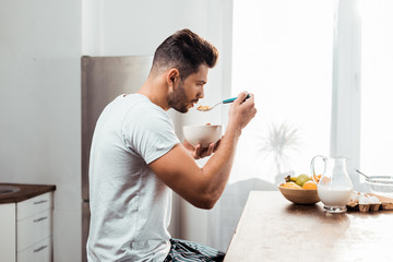 side view of young man in pajamas eating cereals for breakfast at home