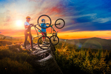 Cycling woman and men riding on bikes at sunset mountains forest landscape. Couple cycling MTB enduro flow trail track. Outdoor sport activity.