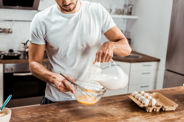 cropped shot of young man pouring milk and cooking omelette at morning