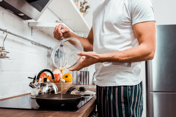 mid section of young man in pajamas cooking omelette on frying pan