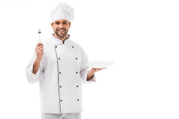 smiling young chef with plate and fork looking at camera isolated on white