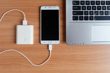 Plug in USB charger from powerbank input mobile phone or cell phone and laptop computer on wooden...