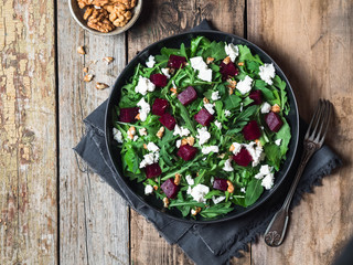 Vegetarian salad of arugula, beet, walnut, feta in a black plate on a wooden board  background. Top view. Copy space
