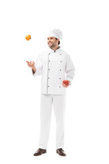 happy young chef juggling with tomato and bell pepper isolated on white