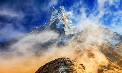 Hiker reaches the summit of mountain peak of Machapuchare. A mountain in the Annapurna Himalayas of north central Nepal. View point from Mardi Himal base camp track