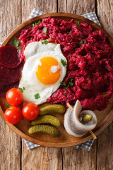 Labskaus is a traditional northern dish of potatoes, corned beef and beets with fried egg, pickles and herring close-up on a plate. Vertical top view