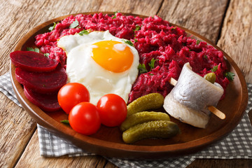 Home-made Labskaus of potato, corned beef and beet served with fried egg, pickles and rollmops close-up on a plate. horizontal