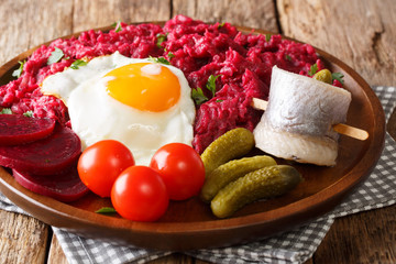 Northern German Labskaus of potatoes, corned beets and beets with a fried egg, pickles and herring close-up on a plate on the table. horizontal