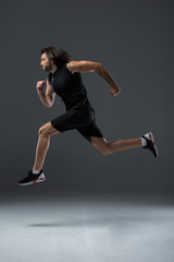 side view of athletic man in earphones running and jumping on grey
