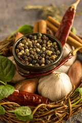 Mix of red, black and white pepper in a black bowl close-up against the background of chili pepper, garlic, cinnamon, onion and other spices