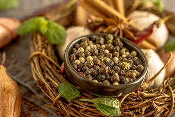 Mix of red, black and white pepper in a black bowl close-up against the background of chili pepper, garlic, cinnamon, onion and other spices