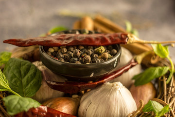 Mix of red, black and white pepper in a black bowl close-up against the background of chili pepper, garlic, cinnamon, onion and other spices