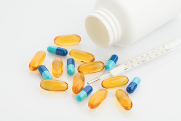 Medical : Close up of Yellow and Blue Capsules with Bottle and Analog Thermometer on 

White Background Shot in Studio.