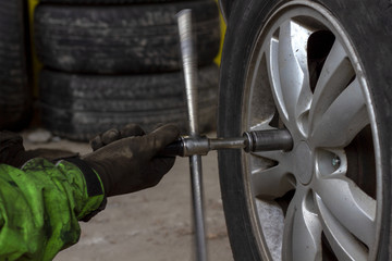 A tire worker unscrews the nuts of an SUV wheel cast disc. A tire worker in a dirty green robe dismantles the wheel of an SUV to replace summer tires with winter tires. © UrbanWitness