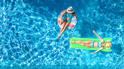Aerial drone view of children in swimming pool from above, happy kids swim on inflatable ring donut and mattress, girls have fun in water on family vacation on holiday resort
