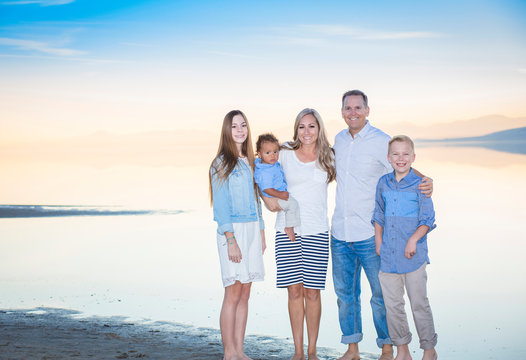 An elegant and beautiful young family portrait at the beach. Smiling and happy diverse group with a mixed race adopted baby boy and two other children. 