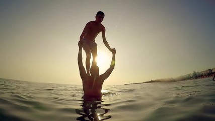 Young man parcour jump backflip from father shoulder in sea at sunset, slow motion