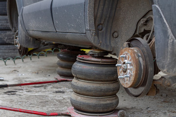 Two lifting jacks raise a dirty SUV with the wheels removed for replacement. Tire replacement in the tire service. Dismantling the wheels in the service station. © UrbanWitness