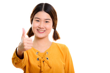 Studio shot of young happy Asian woman smiling while giving thum