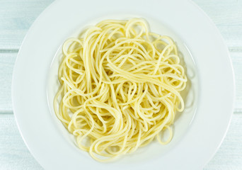 Yellow long spaghetti in a white plate on white wood background.