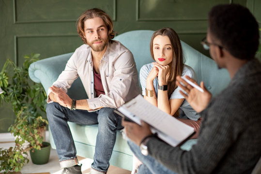 Young serious couple visiting a psychologist sitting on the comfortable couch during psychological session in the green office