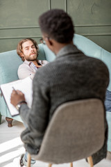 Young caucasian man visiting an african psychologist lying on the comfortable couch during...