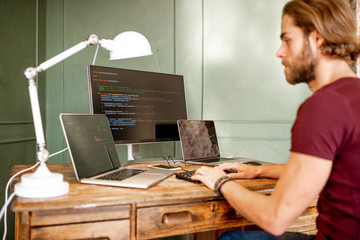 Young programmer writing a program code sitting at the workplace with three monitors in the office...
