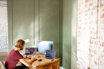 Young programmer writing a program code sitting at the workplace with three monitors in the office...