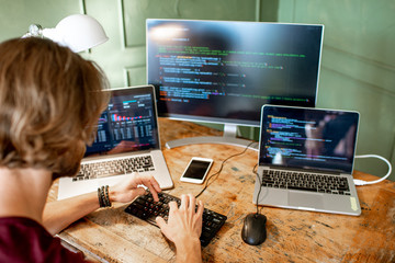 Young programmer writing a program code sitting at the workplace with three monitors in the office